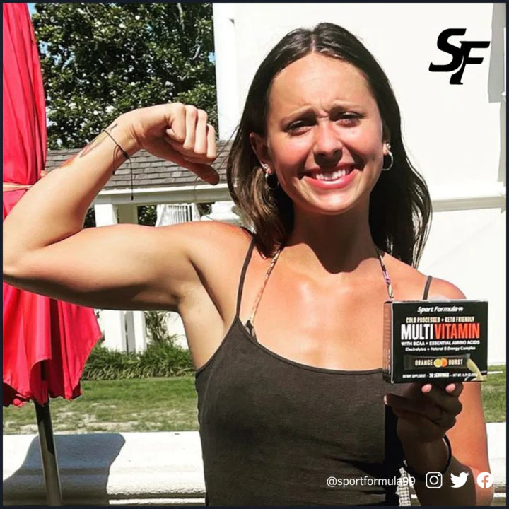 A woman flexes her bicep while holding a box of Sport Formula Multivitamin outdoors, showcasing fitness and health.