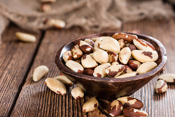 A wooden bowl filled with mixed Brazil nuts, showcasing their distinctive brown and cream-colored shells, on a rustic wooden table.