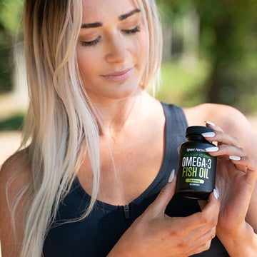 Woman holding a bottle of fish oil and looking at it.