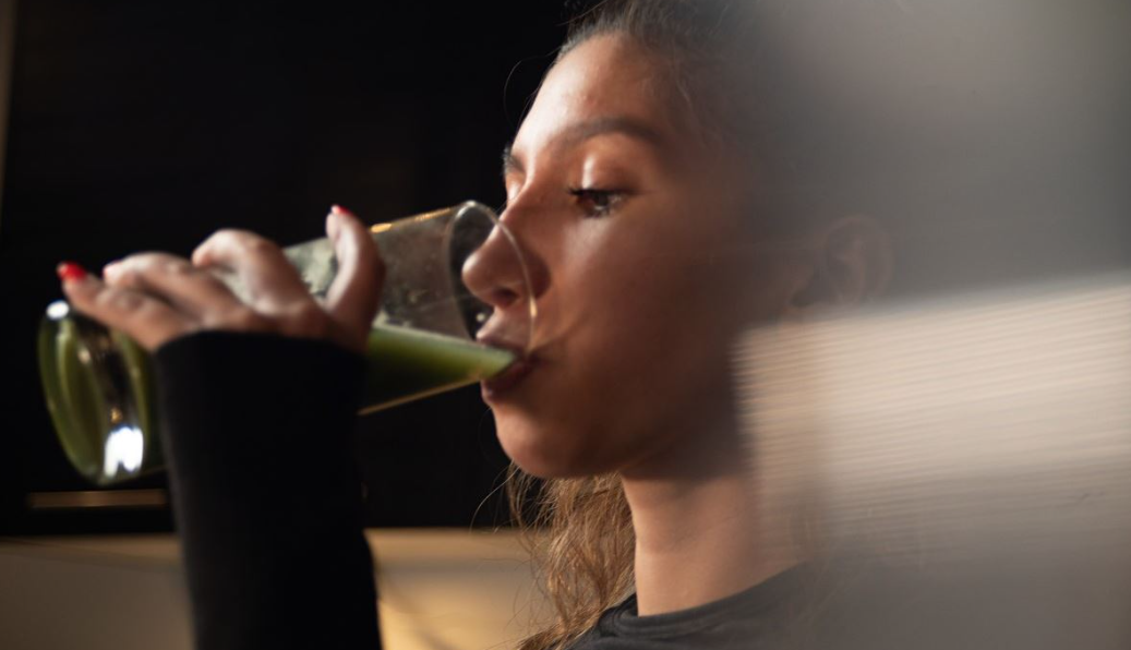 The woman is drinking mixed organic greens from a glass.