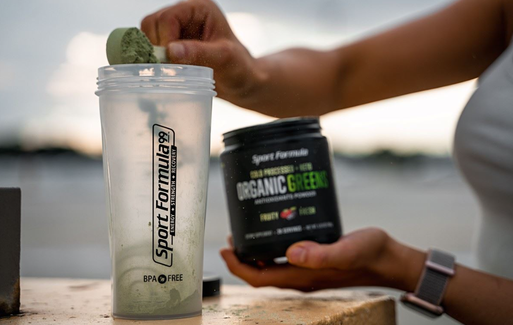 Shaker cup and organic greens while pouring 1 scoop of organic greens.