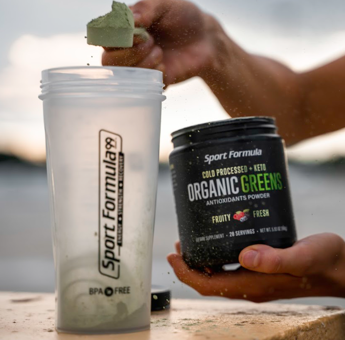 Showing the process of scooping organic greens and adding it to a shaker cup.