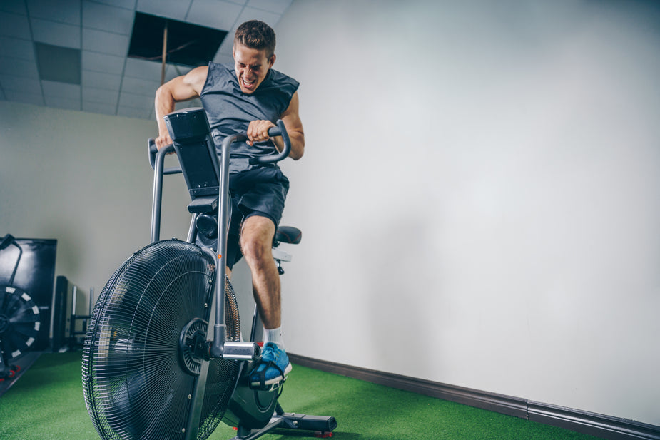 A person is exercising on an air bike in a gym, focusing on fitness amidst a modern, minimalistic environment.