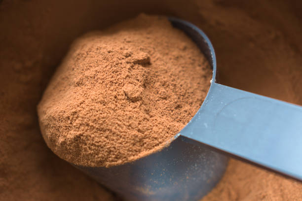 Close-up of a blue measuring scoop filled with brown powder, resting on a dark, textured surface.