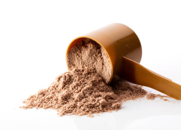 A brown plastic scoop tipped over, spilling protein powder onto a white surface.