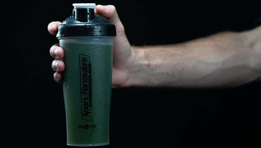 One hand holding a shaker cup with mixed organic greens.