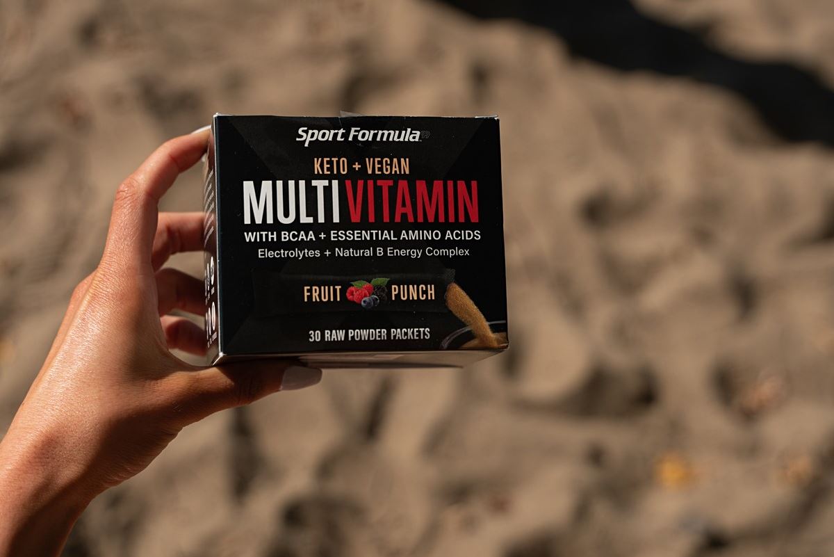 A hand holds a box of Sport Formula's Keto + Vegan Multivitamin, fruity punch flavor, featuring BCAAs and electrolytes.