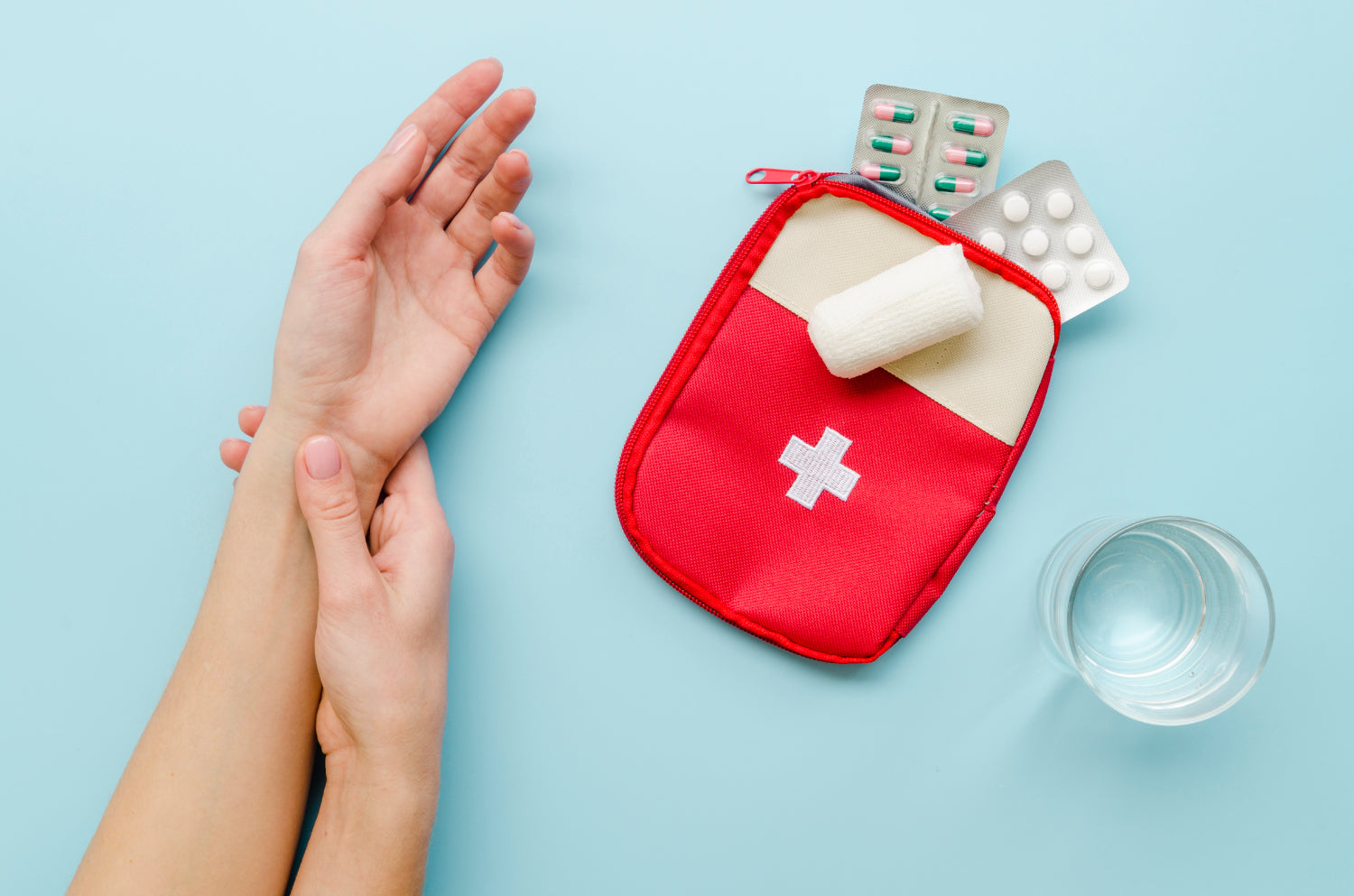 A person's hands are shown holding the wrist, next to a red first aid kit, medication packets, and a glass of water on a blue background.