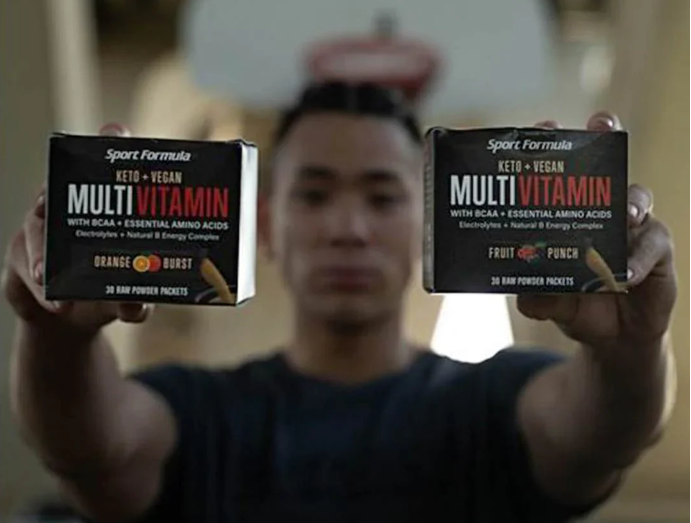 Image of a man holding two multivitamin packets, one labeled 'Orange Burst' and the other 'Fruit Punch'.