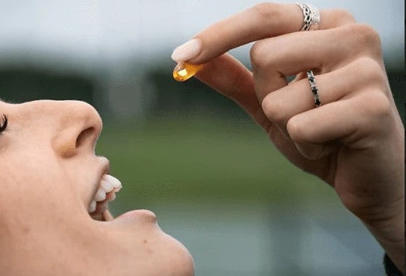 The woman is about to place a piece of fish oil in her mouth.