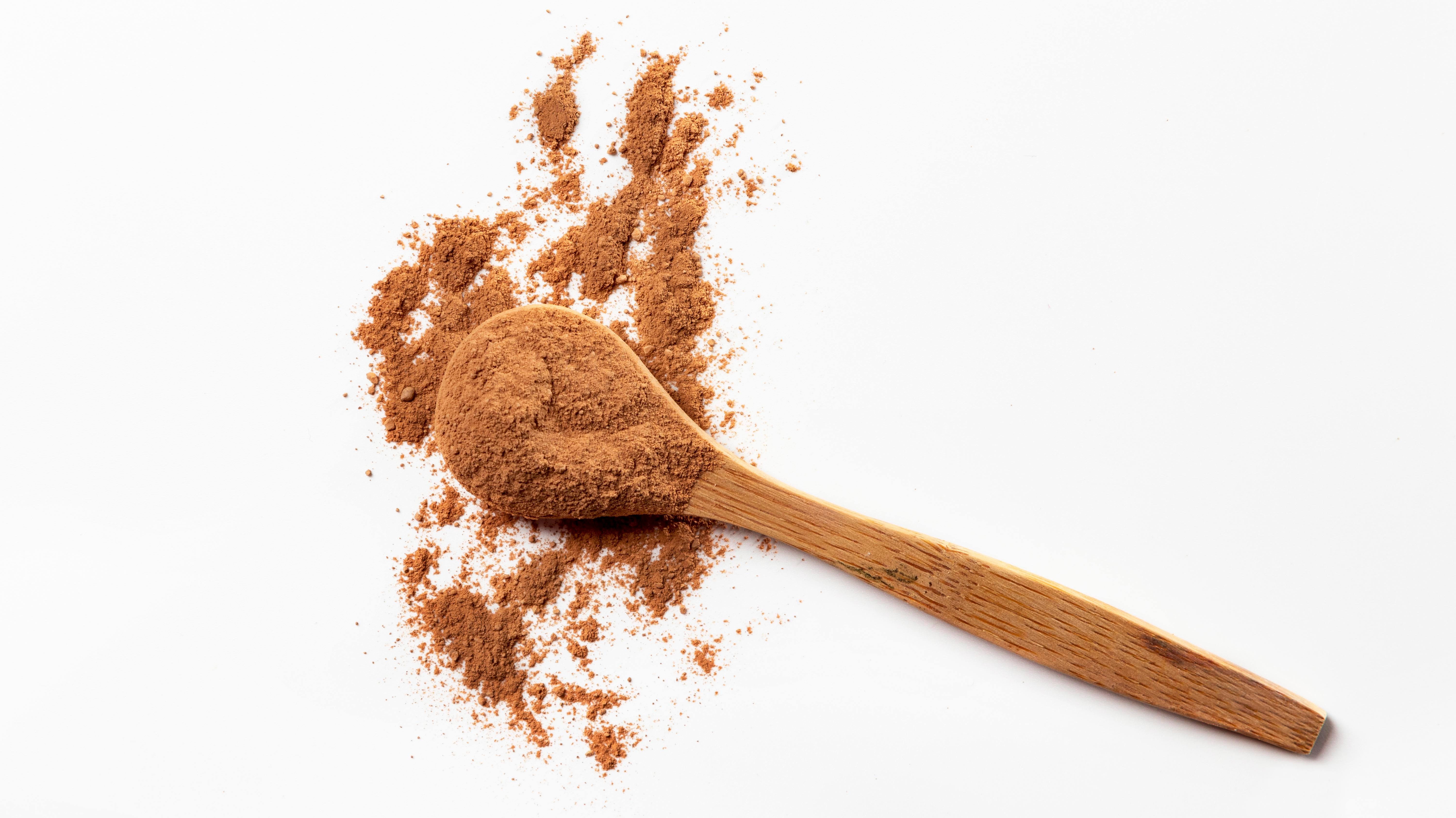 A wooden spoon with chocolate multivitamin powder on a white background.