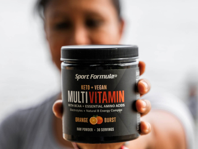 A person holds a jar of keto and vegan multivitamin powder, labeled 