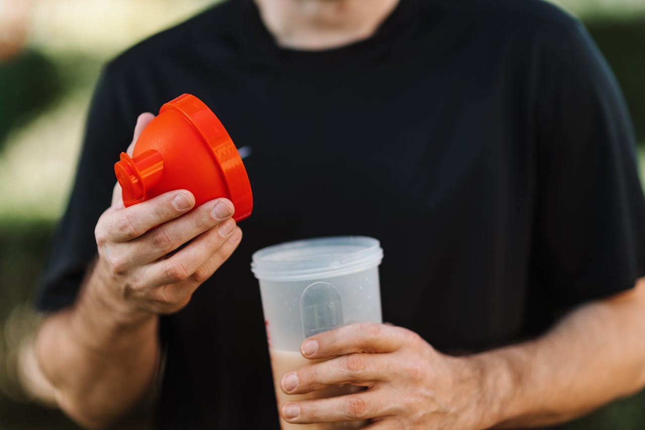 A person in a black shirt holds an orange funnel above a clear shaker cup, preparing to mix a beverage.