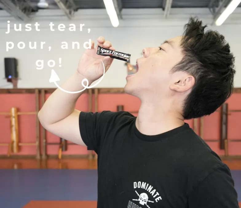 A person tilts their head back, pouring liquid from a tube labeled Sport Formula into their mouth, against a gym background.