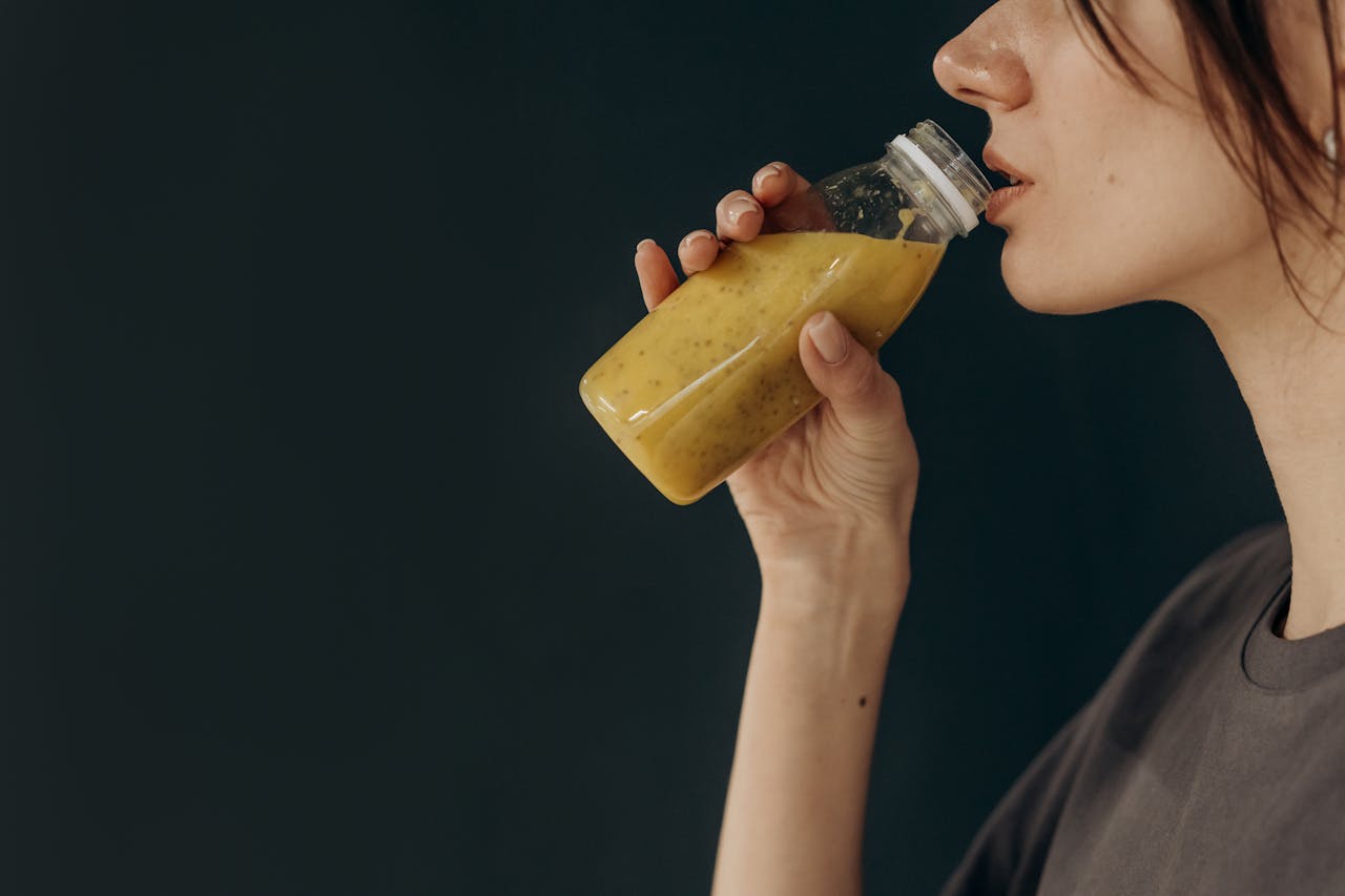 A person holds a glass bottle filled with smoothies, against a dark background, preparing to drink or pour it.