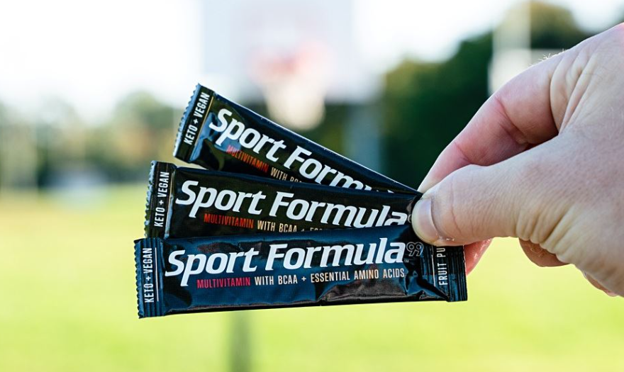 A man holding three packets of Sport Formula Multivitamin Powder drink mix, with the vibrant packaging clearly visible, symbolizing convenience and support for an active lifestyle