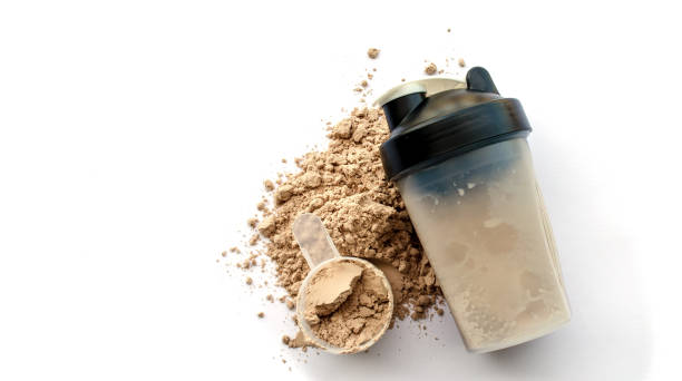 A protein shaker cup next to a scoop and spilled protein powder on a white background.