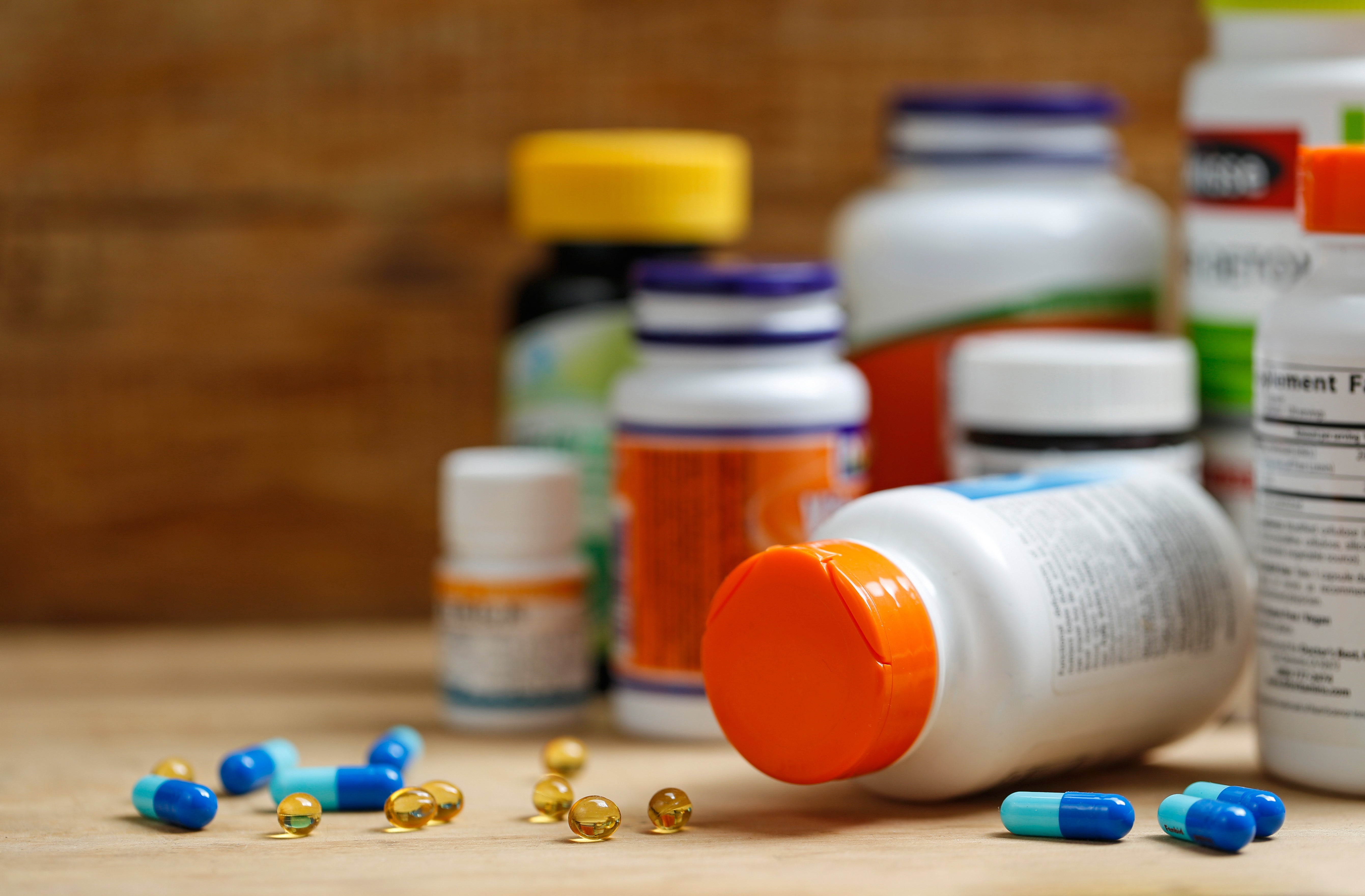 Various supplement bottles with scattered capsules and softgels on a wooden surface.