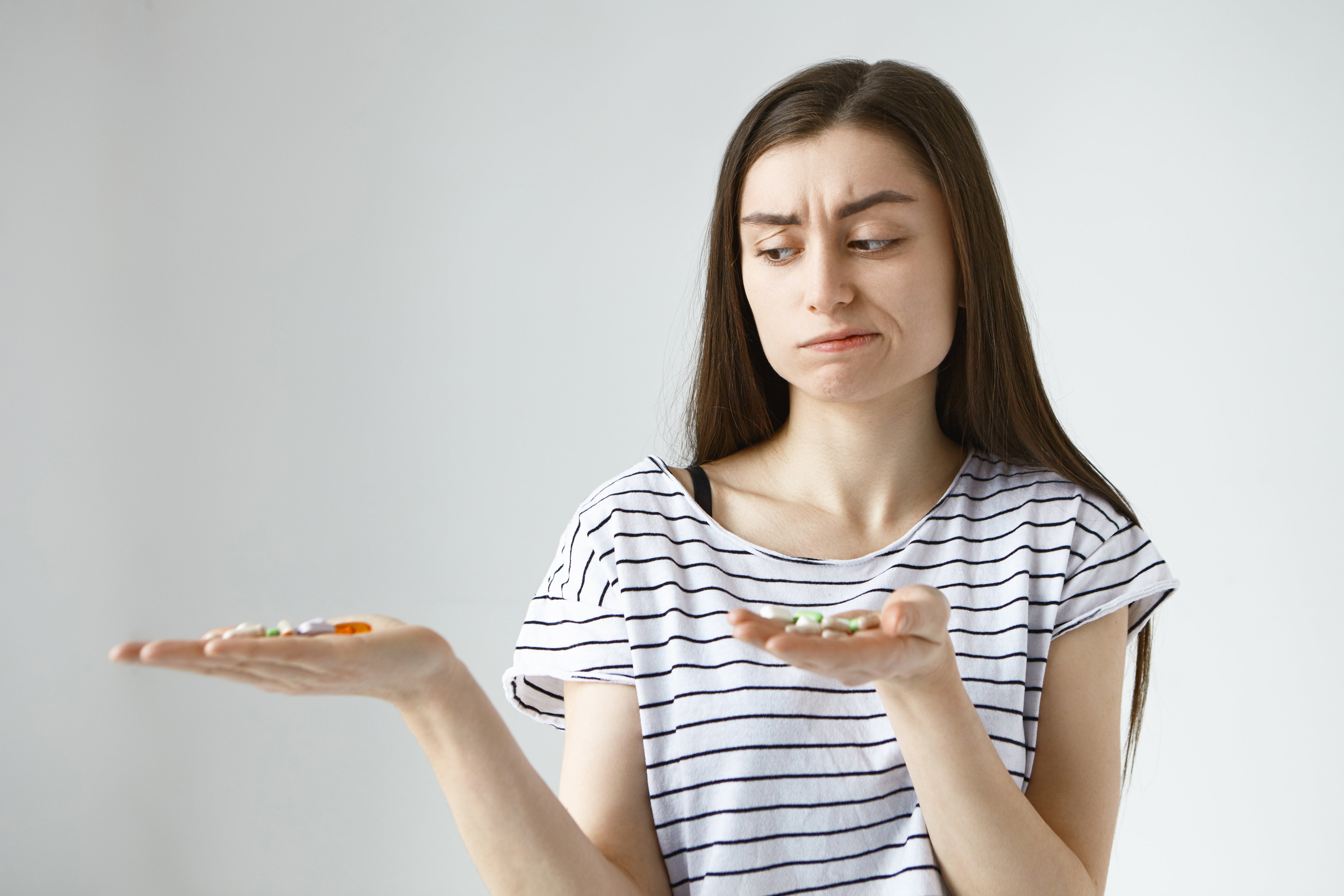 Person in a striped shirt comparing pills on two open palms.