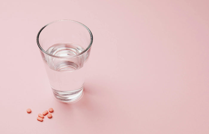 Glass of water with pills on a pink background.