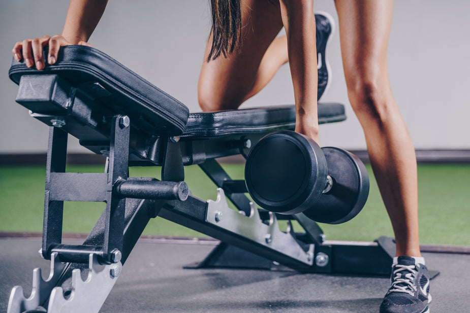 A woman prepares to lift a dumbbell while resting on a weight bench in a gym, showcasing strength training in action.