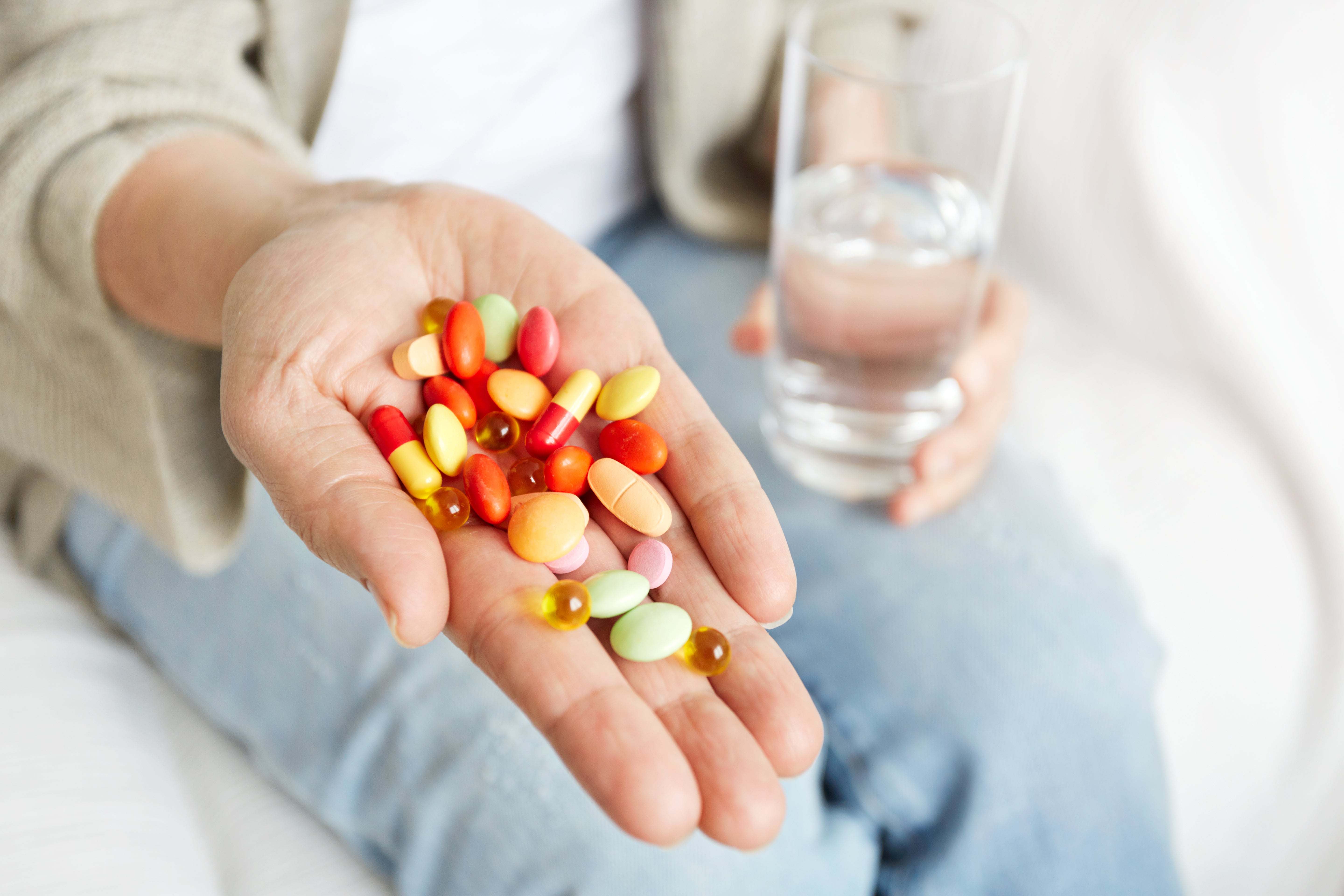 Person holding various colorful pills in one hand and a glass of water in the other.